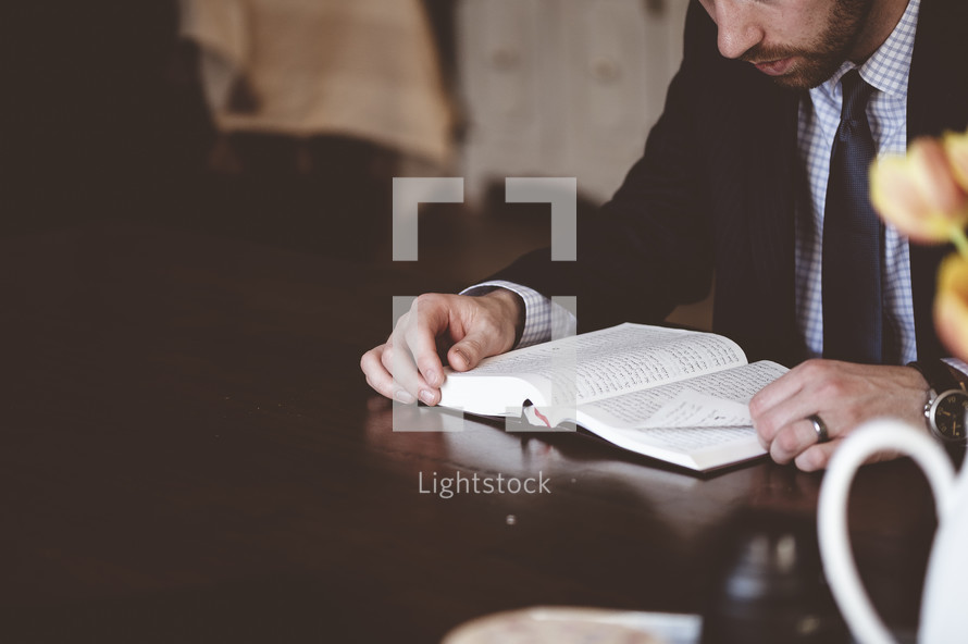 man in a suit sitting at a table reading a Bible 