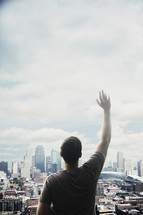 man standing in front of a city with a raised hand 