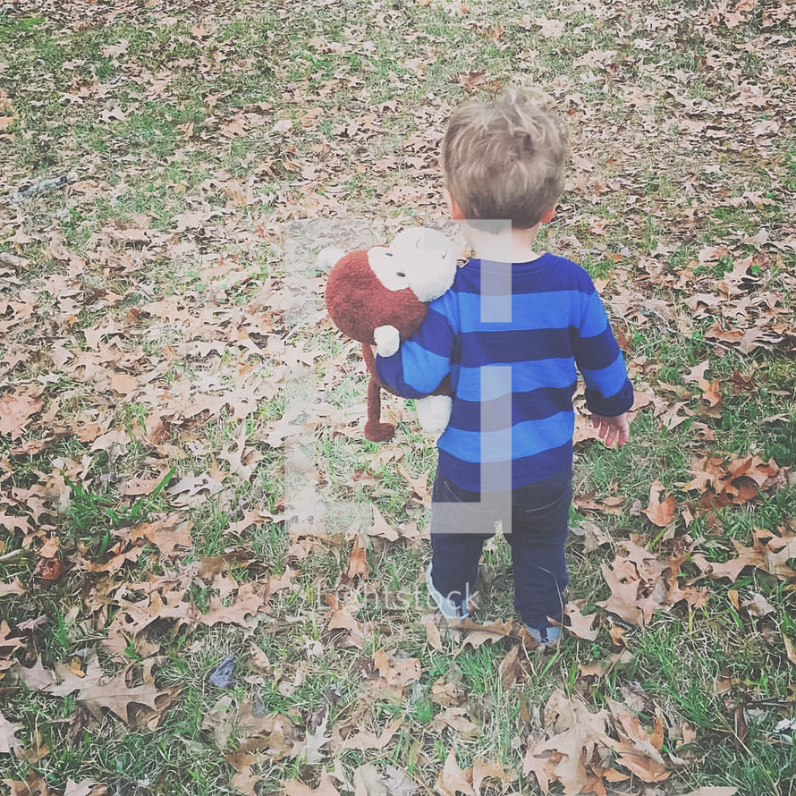 a toddler boy carrying a stuffed animal outdoors 