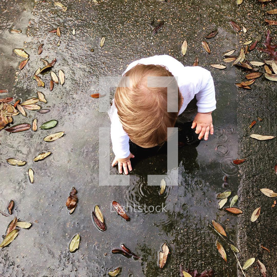 a toddler boy playing in a puddle 