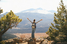 a woman standing on a mountainside with arms raised high 