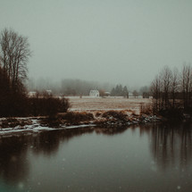 a rural white church across a pond in falling snow 