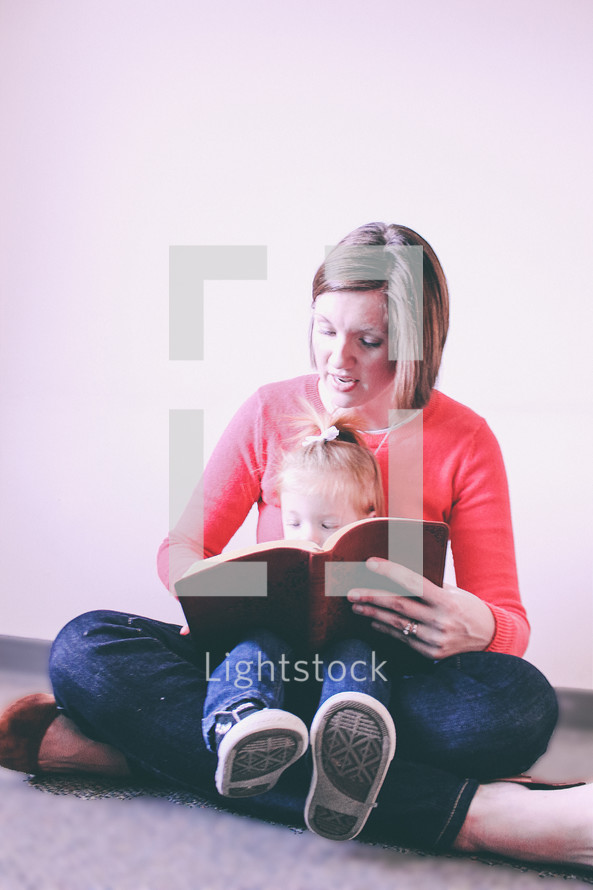A woman reading the Bible to a child in her lap.