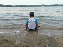 a boy sitting on a beach lake shore 
