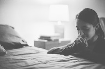 A woman kneeling beside her bed in prayer 