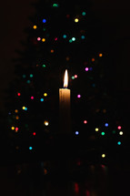 A single candle with flame in front of bokeh colorful Christmas lights