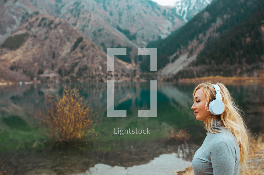 woman listening to headphone with a lake shore 
