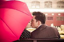 a couple kissing under a red umbrella 