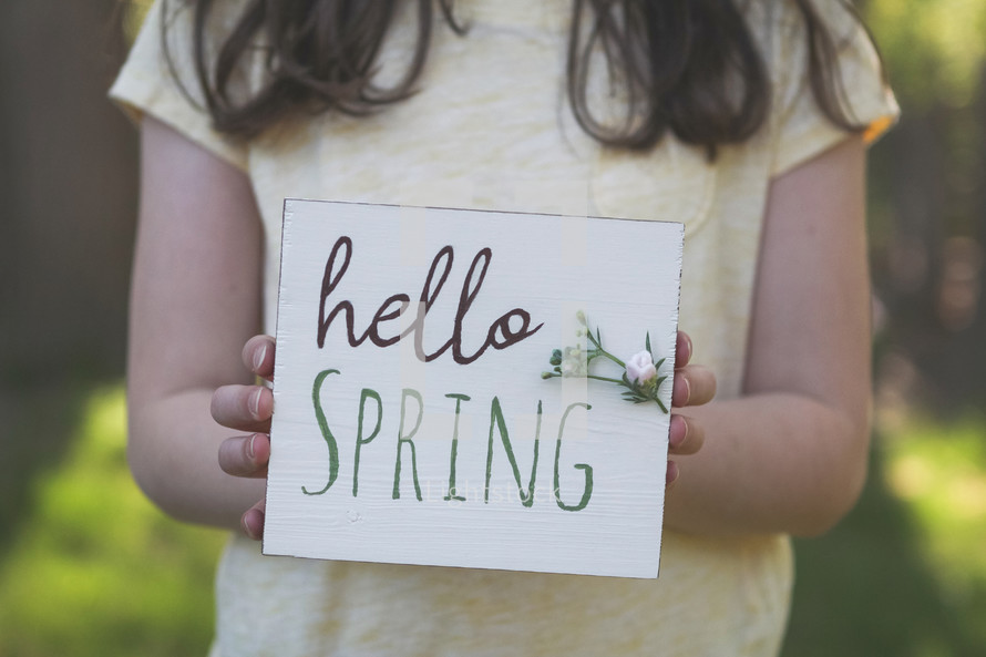 A little girl holding a Hello Spring sign 