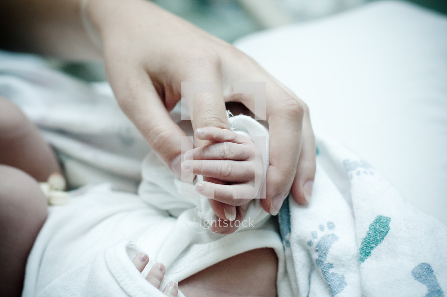 Mother's hand holding hand of newborn infant.