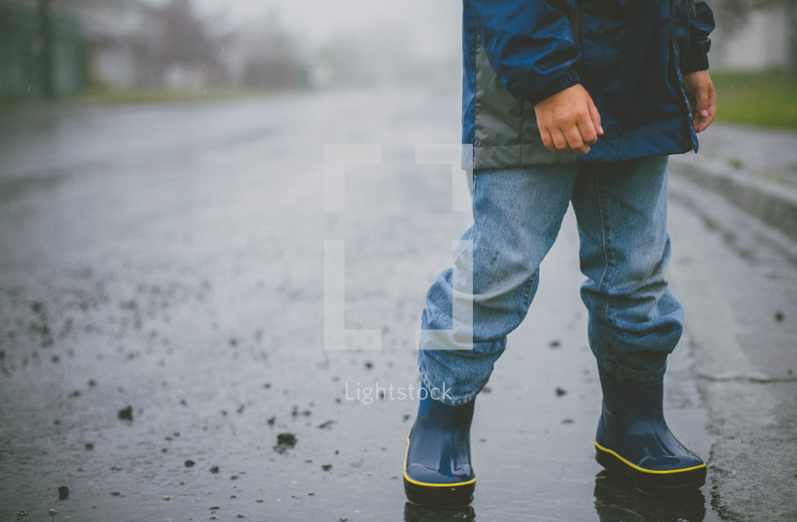 Child in rain boots crossing the wet street.
