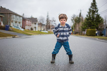 a boy child standing in the middle of a neighborhood street 