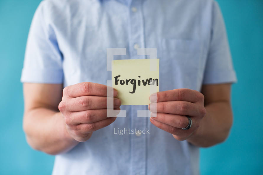 man holding a piece of paper with word forgiven 