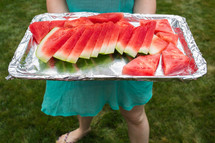 a woman holding a tray of cut watermelon 