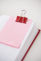 red clip and pink paper on blank journal pages 
