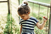 a toddler girl hanging onto a fence 