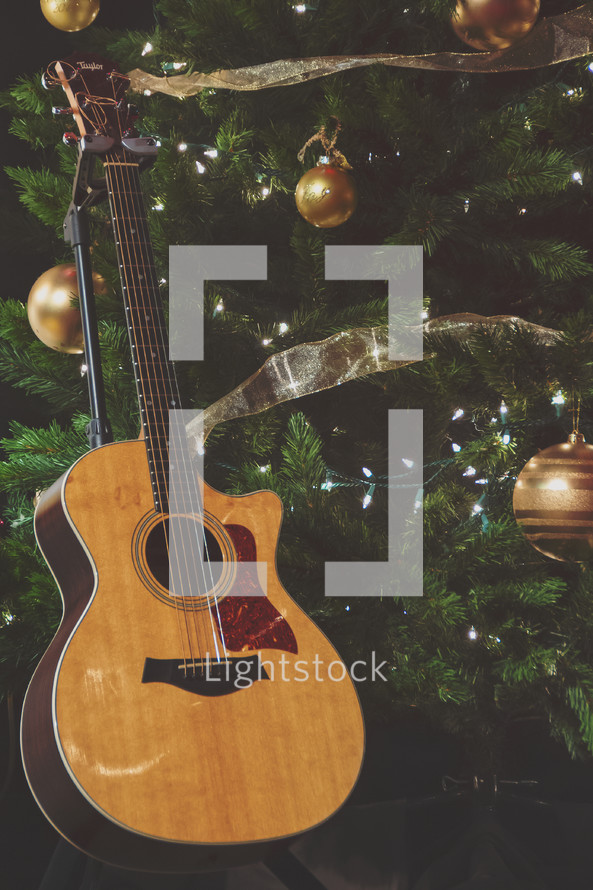 Christmas worship stock photo featuring an acoustic guitar and Christmas tree, ornaments and lights perfect for a social media story background or idea. 