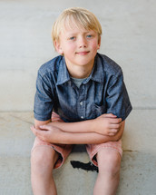 portrait of a young boy sitting on a curb 