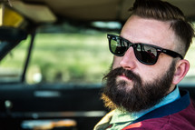 A man with a beard and sunglasses in a car.