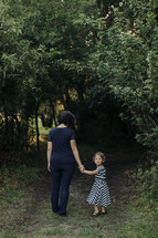 mother and daughter walking holding hands on a path outdoors 