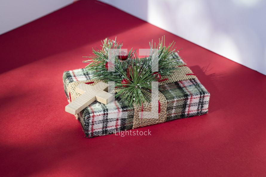 Small wrapped Christmas present with cross on red table