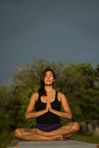a woman meditating outdoors under a cloudy sky 