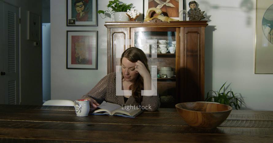 a woman sitting at a dining room table reading a Bible 