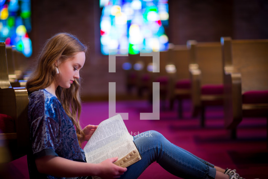 Young woman or teen sitting in aisle of a church meditating on scripture.