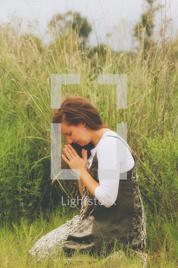 a young woman kneeling in a field praying 