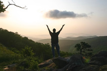 a man standing on a mountaintop with hands raised 