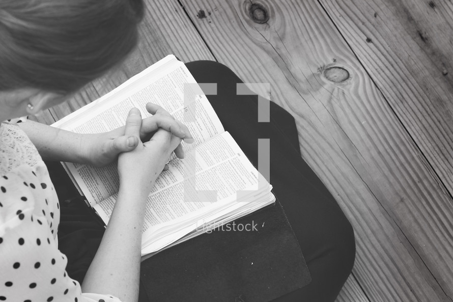 woman sitting with praying hands over a Bible 