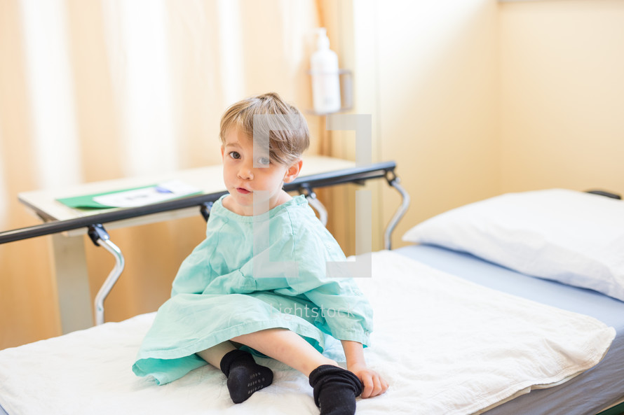 a boy child in a hospital gown on a stretcher 
