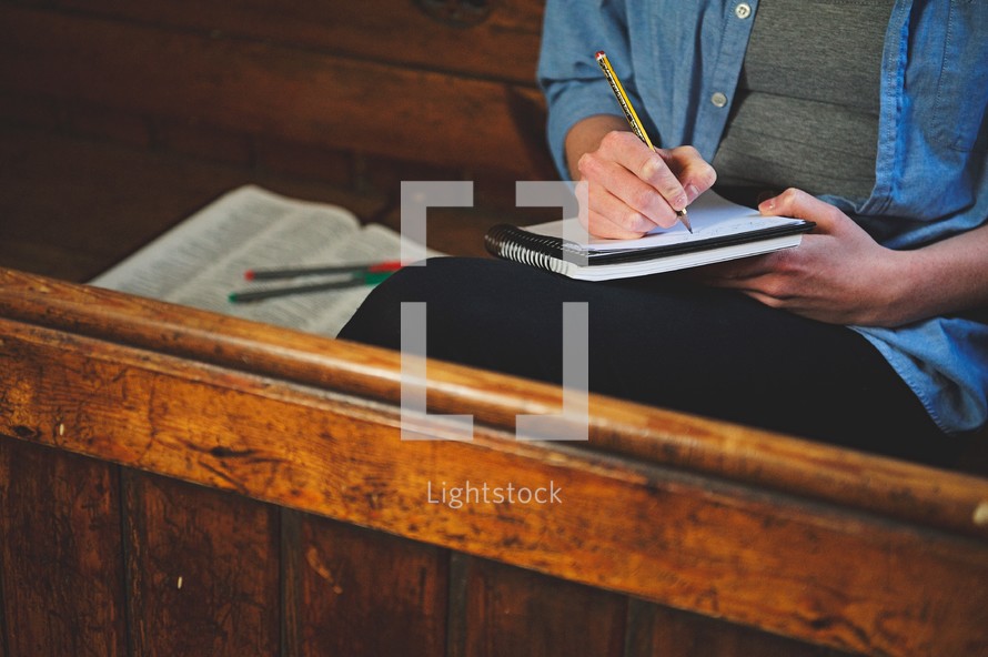 a woman writing in a notebook while sitting in a church pew 
