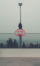 teen boy sitting on a basketball goal 
