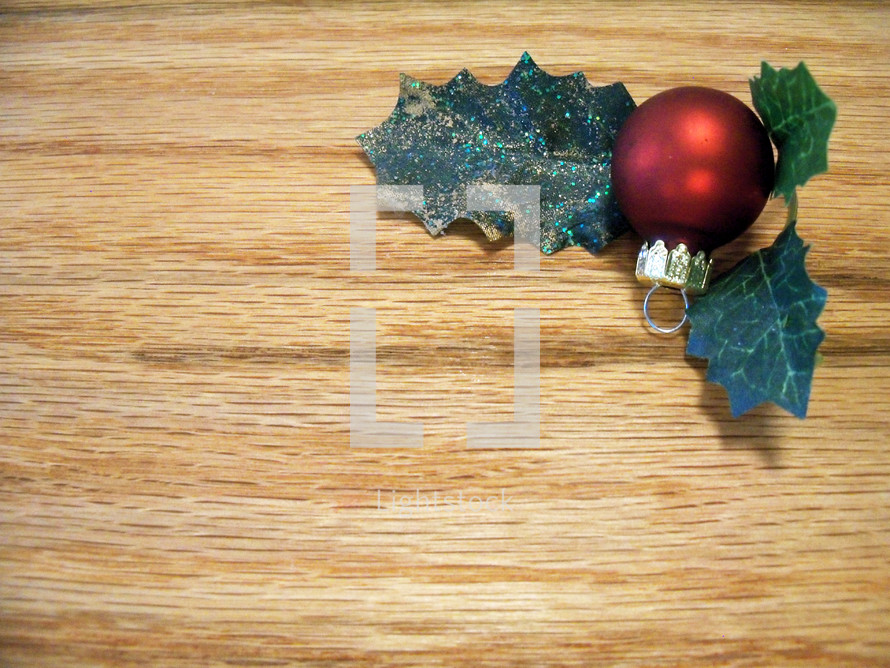 A Christmas background with wood grain and a Christmas ball ornament and holly leaves in the upper right hand corner. Background image used for articles, websites or Church bulletins.