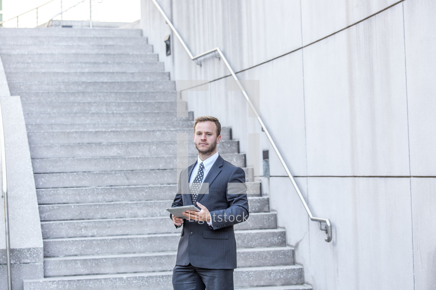 portrait of a businessman holding a tablet in front of stairs 