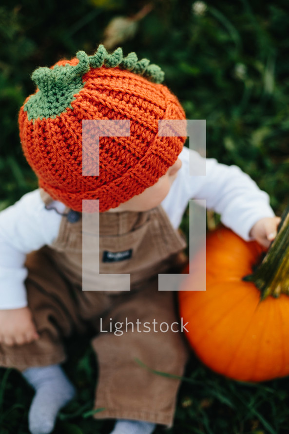 toddler in overhauls with a pumpkin 