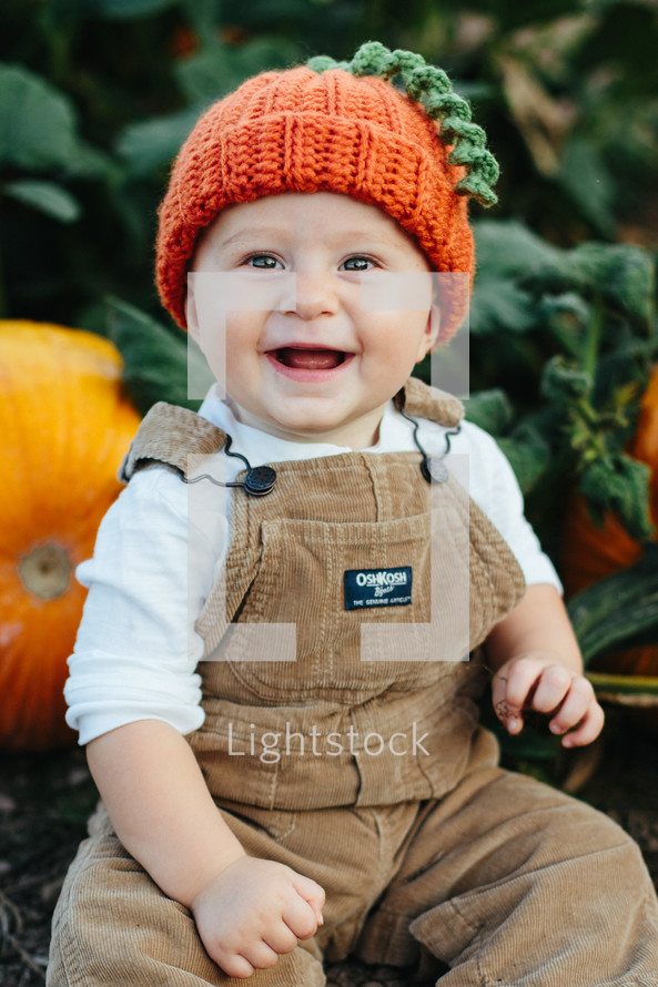 toddler in overhauls with a pumpkin 