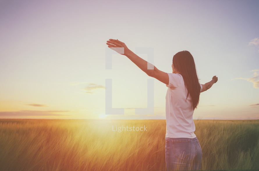 woman standing in a golden field with outstretched arms 