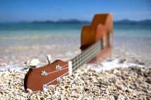 Guitar in the sand on the beach by the ocean.