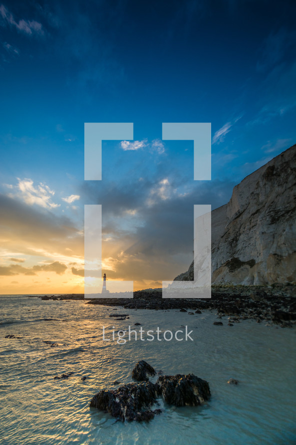 Seaside cliffs with a lighthouse and sunset in the distance.