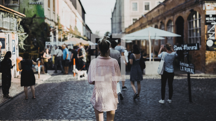 a woman walking into a street market on a cobble stone street 