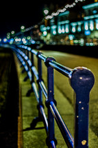 A blue railing along a street at night.