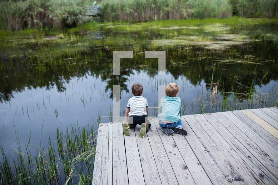 children looking at pond water from a dock 