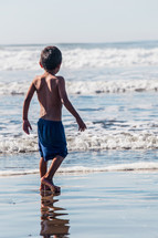 boy child walking in wet sand on a beach 