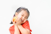a little girl in a traditional Chinese dress holding an orange 
