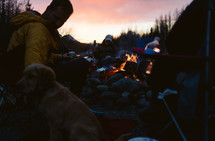 Friends and their dog around a campfire at sunset