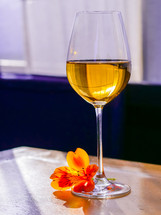 Glass of white fine wine with flower on vintage shabby wooden table in restaurant.