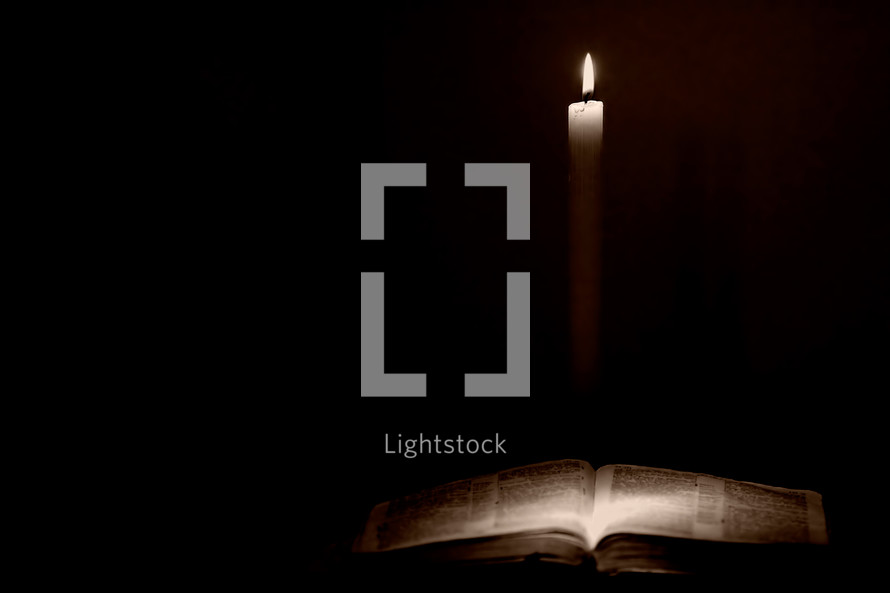 A well-used Holy Bible is lit by a single candle in a vintage style - Shallow depth of field.