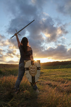 A warrior woman raises her sword in victory in the light of a sunset.